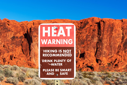 Extreme Heat warning sign informs tourists of the dangers of heat exhaustion from hiking in the desert climate. Blurred scenic red sandstone formations and desert scrub landscape background. Blue sky.