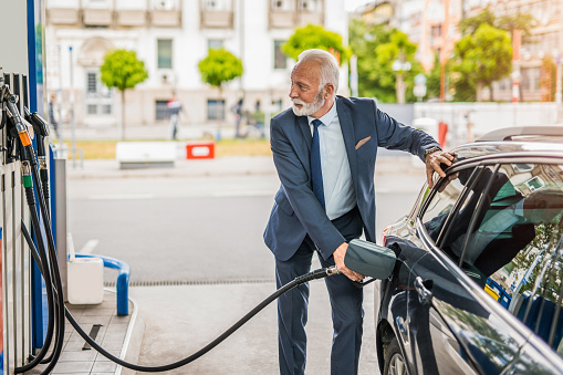 Senior businessman sipping fuel into his car tank at the gas station.