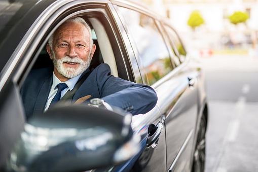 Happy senior businessman sitting in his daily commuter and looking at camera.