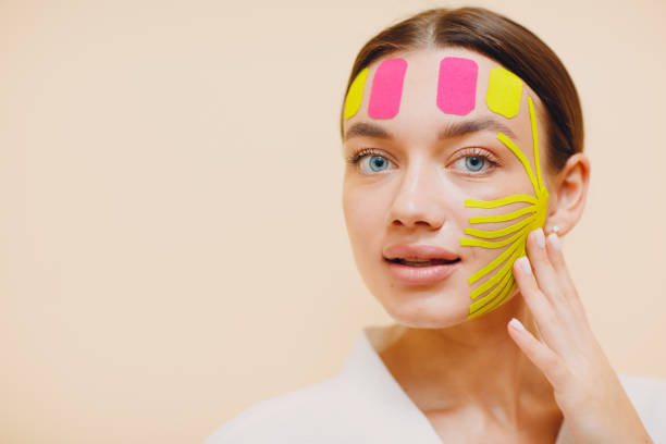 hermosa mujer aplicando tratamiento de elevación de cinta en la cara - kinesio fotografías e imágenes de stock