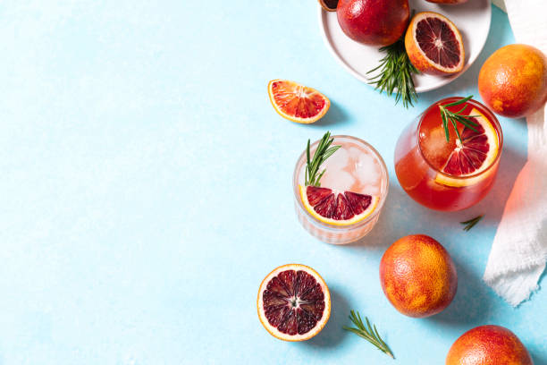 Blood orange cocktails with fresh fruits on blue table background. Summer cocktails, lemonade, refreshing drinks, low alcohol mocktail, party concept. Flat lay, top view, copy space. stock photo