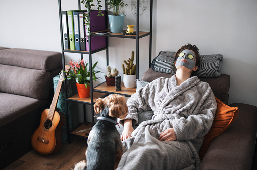 Woman with a facial mask relaxing at home with her dog next to her