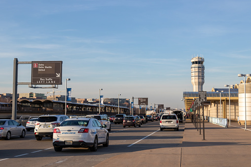 Traffic is seen arriving at Ronald Reagan Washington National Airport, Terminal B/C on a busy afternoon. A police potrol car is stopped on the forground with the iconic air traffic control tower is in the background.