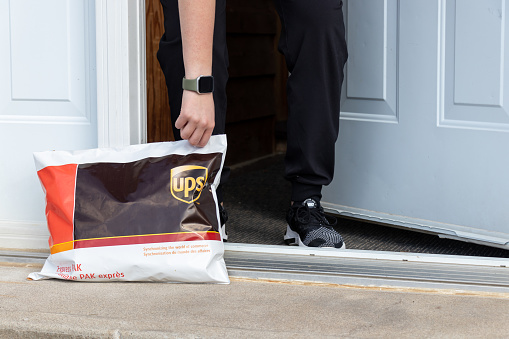 A United Parcel Service aka UPS package left at the front door of a person's home is picked up from the front steps. UPS is one of the world's largest shipping couriers, delivering globally to over 100 countries.