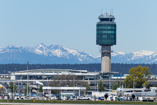 The Air Traffic Control tower of Vancouver International Airport (YVR) managed by NavCanada is seen from a distance with the snow-covered mountains of British Columbia.