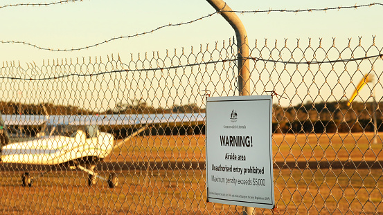 A close up of the Commonwelath of Australia warning sign at a regional airport or airfield. No unauthorised sign on a chicken wire security fence and barbed wire.