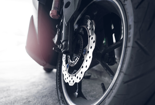 Closeup disc brake of a scooter. Aluminum alloy wheel of motorcycle. Steel rims. Mag wheels of motorbike. Performance wheel and tire of motorcycle. Chrome disc brake and abs. motorbike accessory.
