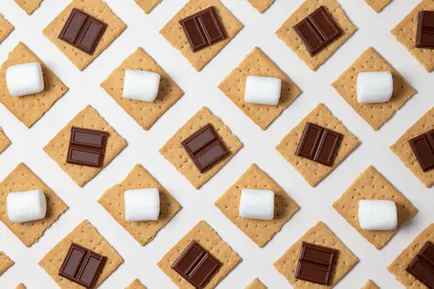 graham cracker squares with  chocolate bars, marshmallows on a white background.