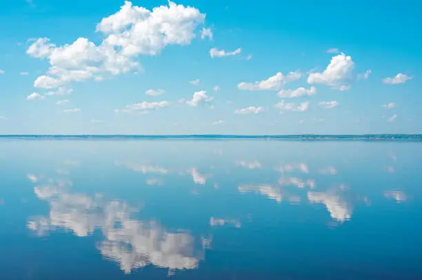 Photo of cloudscape. clouds in blue sky and reflection in a large lake. White cumulus clouds in sky over blue sea water landscape, big cloud above ocean panorama, horizon, sunny summer day seascape panoramic