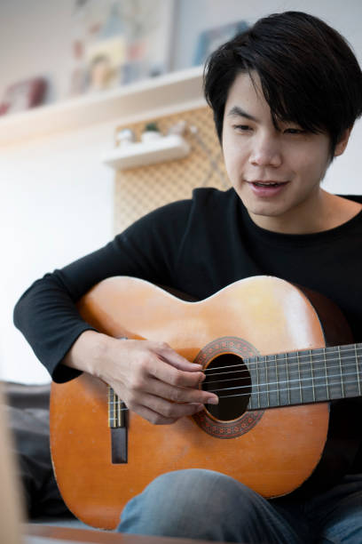 istock Portrait of happy man playing guitar on sofa. 1323803572