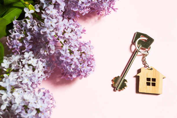 house key with keychain on pink spring background and lilac branches. summer holiday home, booking cottage in the countryside, moving to new home, mortgage, rent and purchase real estate. copy space - key real estate key ring house key imagens e fotografias de stock