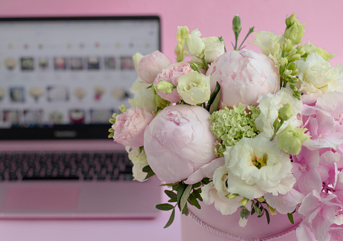 bouquet of flowers in a box close-up, against the background of an open laptop. Selective focus. Hydrangea, roses and peonies on a pink background. home delivery concept, buying flowers online.