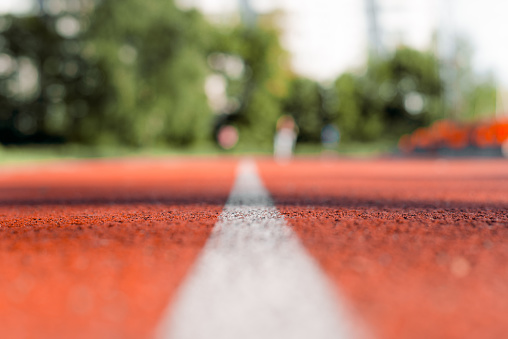 Outdoor stadium jogging track. Texture of red rubberized surface with a white line in the middle. Running track close-up. Selective focus, blurred background.