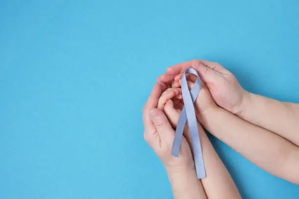 grandmother and granddaughter hold a blue ribbon on a blue background, child's hands and woman's hands, copy space , diabetes and cancer symbol