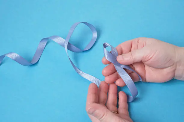 grandmother and granddaughter hold a blue ribbon on a blue background, child's hands and woman's hands, copy space , diabetes and cancer symbol
