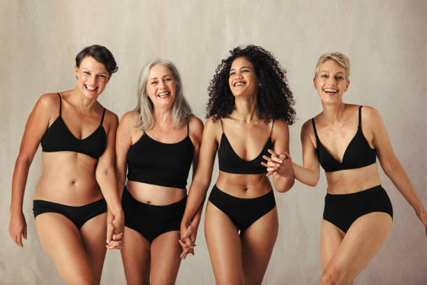 Female models of different ages celebrating natural bodies Female models of different ages celebrating natural bodies. Four body positive and confident women smiling cheerfully while wearing black underwear and holding hands together in a studio. the human body stock pictures, royalty-free photos & images