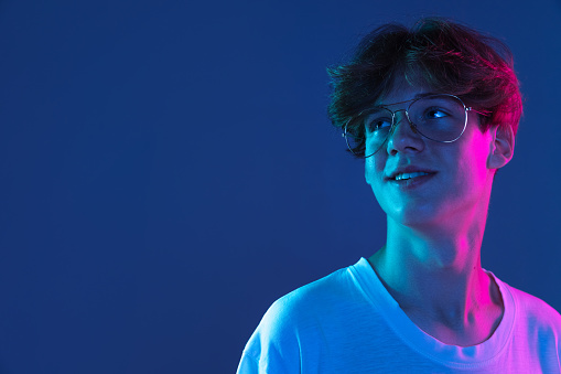 Smiling. Caucasian young man's portrait on dark studio background in neon light. Handsome male model in casual style. Concept of human emotions, facial expression, youth, sales. Copy space for ad.