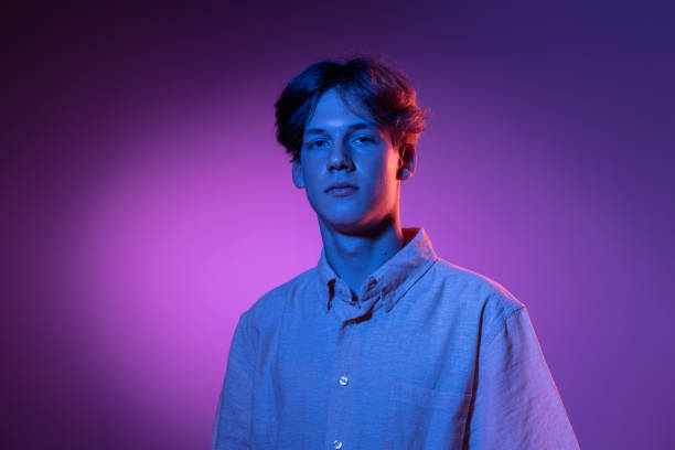 Serious. Handsome caucasian man's portrait isolated on purple studio background in neon, monochrome. Beautiful male model. Serious. Handsome caucasian man's portrait isolated on purple studio background in neon, monochrome. Beautiful male model. Concept of human emotions, facial expression, sales, ad, fashion and beauty. neon portrait boy stock pictures, royalty-free photos & images