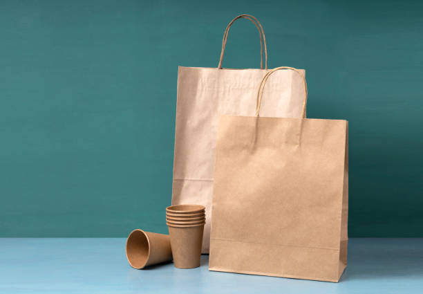 istock Paper bags and cups on the blue surface against green background.Empty space 1323839315