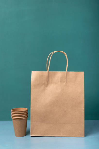 immagine verticale del sacchetto di carta e pila di tazze di carta sul tavolo blu contro la parete verde - disposable cup cup stack blue foto e immagini stock