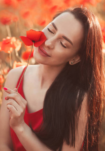 젊은 갈색 머리 여자 25-30 세 와 긴 손질 머리 에 빨간 드레스 에 a 양귀비 꽃 에 필드 - cosmetics young women human skin 25 30 years 뉴스 사진 이미지