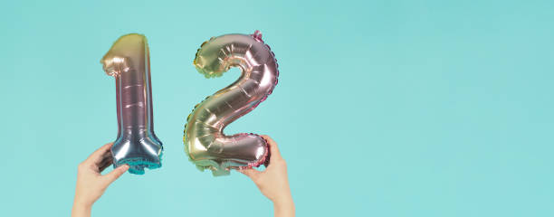 istock Hand is holding balloon number 1 2 or twelve on mint or tiffany blue background. 1323843933