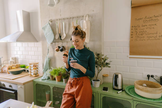 Healthy snack in my kitchen Photo of a young smiling woman having healthy snack in her kitchen eating stock pictures, royalty-free photos & images