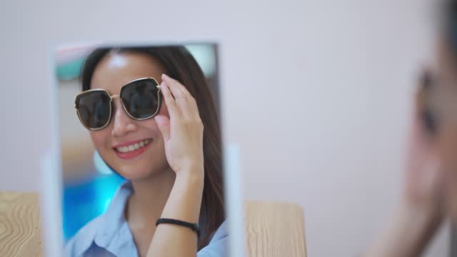 Asian chinese beautiful woman trying on sunglasses in front of mirror at optician store