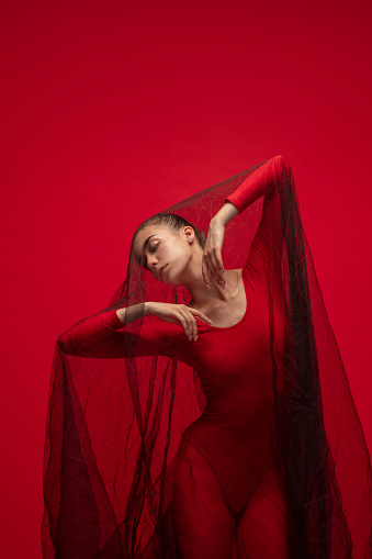 Art performance. Graceful young beautiful girl, female ballet dancer posing isolated on red background. Lady in red. Concept of beauty, art, show, theater. Contemporary ballet. Copy space for ad.
