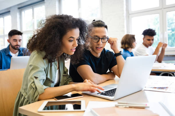 Classmates are learning through laptop Young curly hair woman discussing with man in classroom. Classmates are learning through laptop. They are wearing casuals. adult student stock pictures, royalty-free photos & images