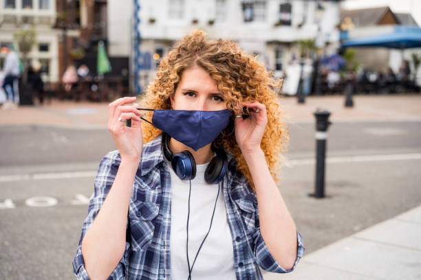 Young happy caucasian woman takes off a protective face-covering mask outdoors against European city background. Pandemic Covid-19 is over concept. Selective focus. Young happy caucasian woman takes off a protective face-covering mask outdoors against European city background. Pandemic Covid-19 is over concept. Selective focus happy end stock pictures, royalty-free photos & images