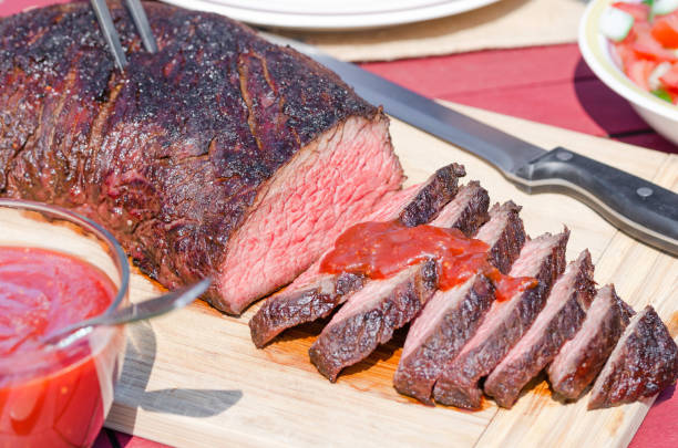 Grilled Tri Tip Steak and Barbecue Sauce Cooked beef tri-tip sliced, also known as aiguilette baronne in France, on wooden cutting board, served with homemade BBQ sauce made with tomato and fresh vegetable salads for barbecue season boneless chuck steak stock pictures, royalty-free photos & images