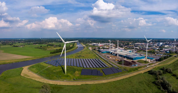 オランダの河川景観における持続可能な産業の一部であるオランダの風力タービン、水処理およびバイオエネルギー施設とソーラーパネルのパノラマビュー。 - industrial windmill ストックフォトと画像