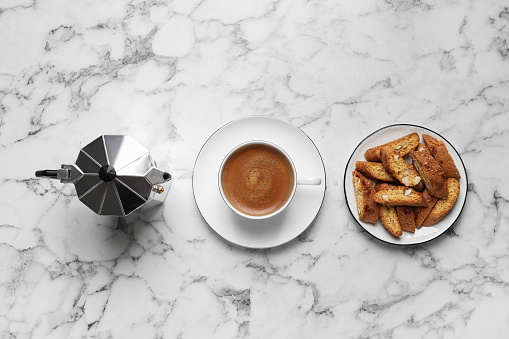Tasty cantucci, cup of aromatic coffee and moka pot  on white marble table, flat lay. Traditional Italian almond biscuits