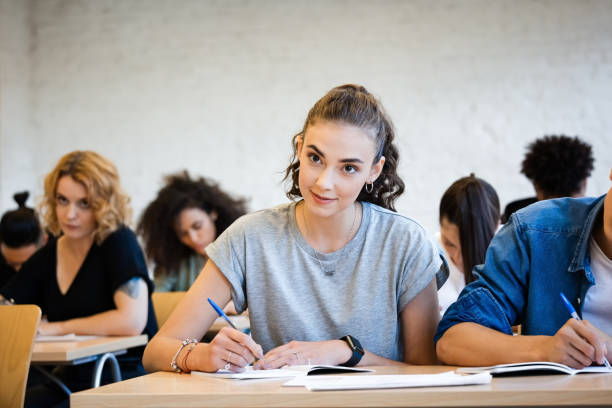 istock Young woman writing in book while sitting at desk 1323856678