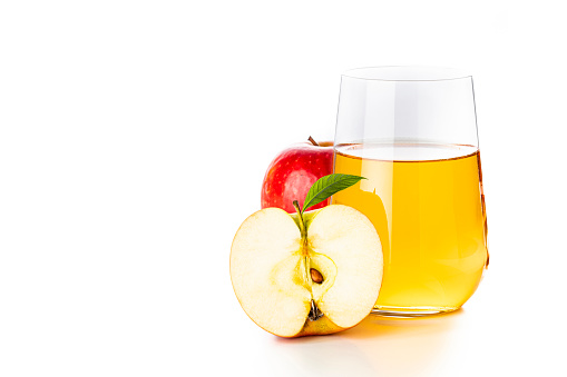 Front view of a single drinking glass full of apple juice beside a sliced and a whole red apple isolated on white background.