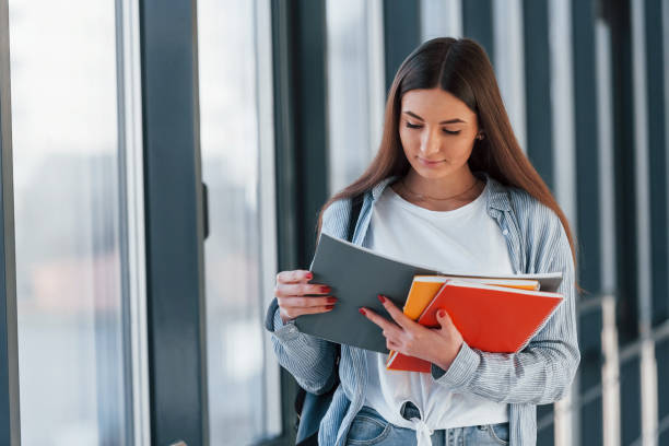 istock Female young student reading information from notepad in corridor of a college 1323860268
