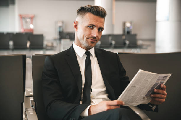 Smiling businessman reading newspaper Smiling businessman reading newspaper while sitting at the airport terminal lobby newspaper airport reading business person stock pictures, royalty-free photos & images