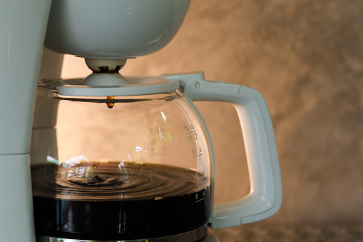 Cafetera con café goteando en el interior sobre fondo de hormigón gris y luz cálida. Espacio de copia. photo