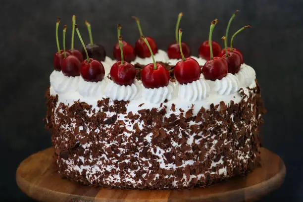 Stock photo showing a homemade, luxury, Black Forest gateau displayed on a metal and wood cake stand against a black background.