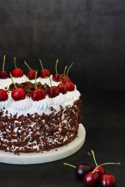 Stock photo showing a close-up, elevated view of a homemade, luxury, Black Forest gateau displayed on a marble cake stand against a black background.