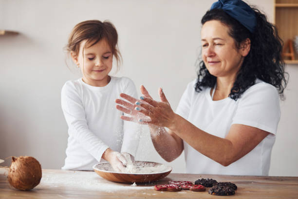 台所で小麦粉で食べ物を準備する孫娘を持つ先輩女性 - grandmother senior adult family domestic kitchen ストックフォトと画像