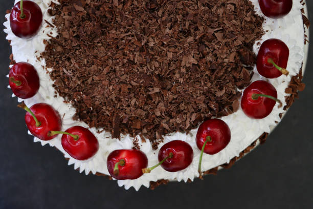 istock Image of Black Forest gateau with piped whipped cream rosettes topped with morello cherries, luxury chocolate cake frosted with whipped cream and covered with chocolate shavings, black background, elevated view 1323862394