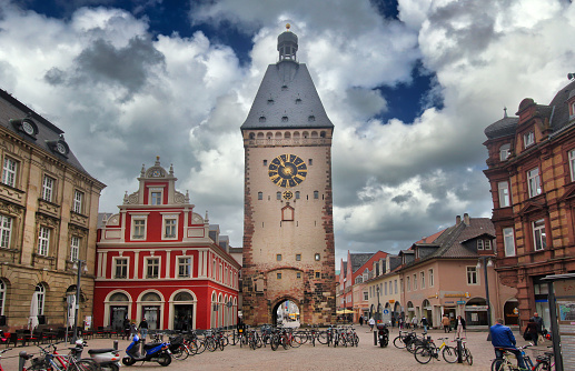 Speyer, Germany - May 2, 2014: Tourists walk and make pictures in the plaza in front of the old clock tower and a red house in the old centre of Speyer, Germany on May 2, 2014