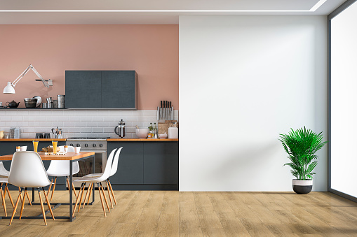 Empty anthracite modern kitchen on hardwood floor with appliances, full dining table, chairs in front of a partly white tiled wall and partly pink plaster wall. A potted plant in front of a large white plaster wall background with copy space and windows on a side. 3D rendered image.