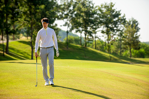 Asian man golfer  holding golf club walking  on fairway at golf course  , Sport healthy holiday lifestyle  Concept