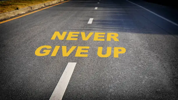 Photo of Never give up word on asphalt road surface with marking lines