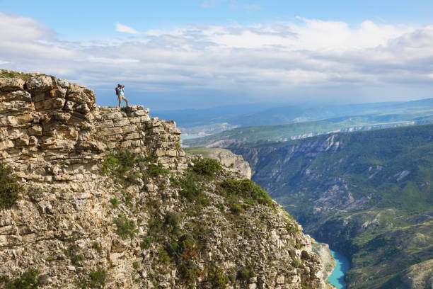 istock Young woman backpacker standing on cliff's edge and taking a photo 1323870110