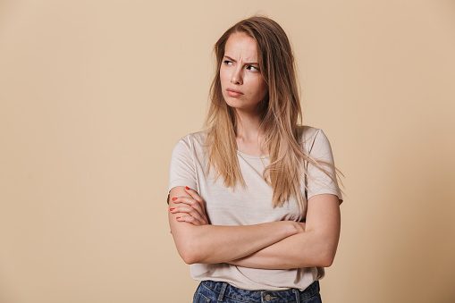 Portrait of an upset casual girl with arms folded looking away isolated over beige background