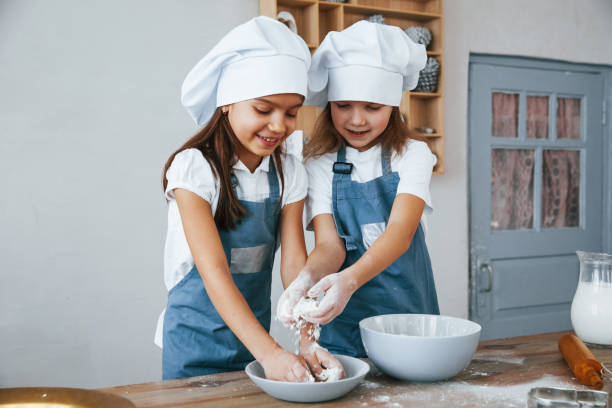 istock Two little girls in blue chef uniform working with flour on the kitchen 1323873620